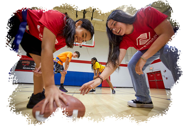 Two girls and a football in a gymnasium.